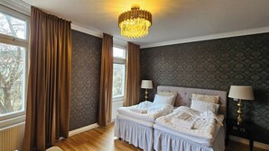 Une chambre avec deux lits, un lustre et une vue sur les arbres à travers de grandes fenêtres.