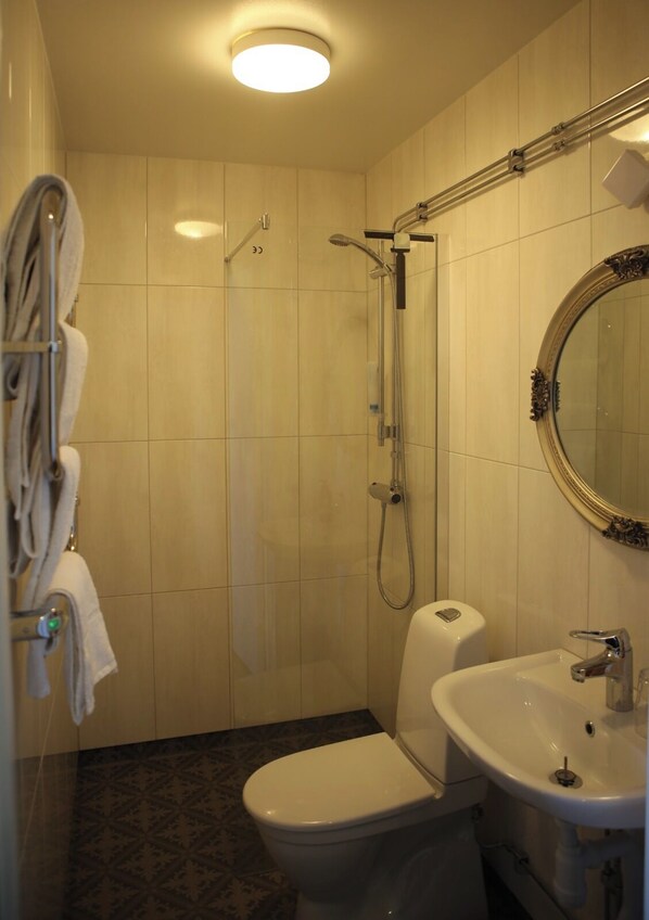 A bathroom with a toilet, sink, shower, and a mirror.