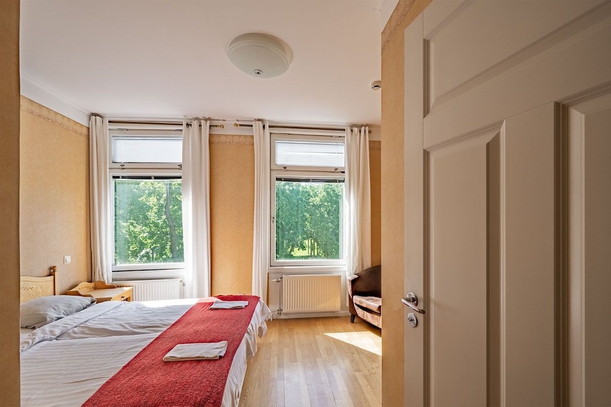 A bedroom with a bed, two windows, a radiator, and a door.