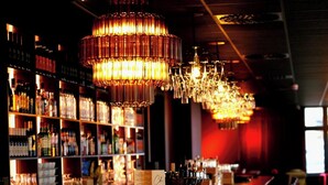 Un bar doté de plusieurs lustres suspendus, d’étagères remplies de bouteilles et d’un présentoir à menus.