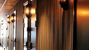 Un couloir d’hôtel avec des portes, chacune étant surmontée d’un luminaire.
