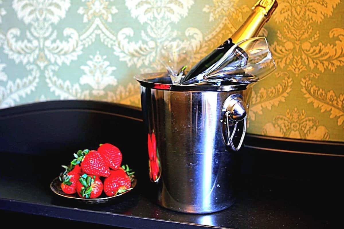 Un cubo de champán de acero inoxidable con una botella y una copa, junto a un cuenco de fresas.