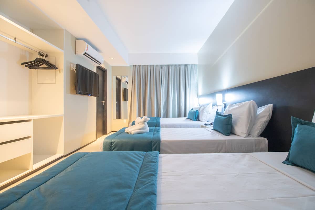 Quarto de hotel com duas camas, um guarda-roupa, uma televisão e um ar condicionado.