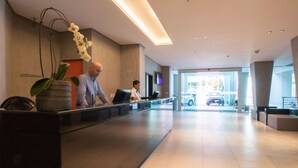 A modern reception area with a reception desk, a large potted orchid, and a glass door leading outside. - Acqua Prime (Maceió)