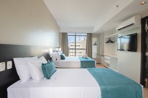 Ein Hotelzimmer mit zwei Betten, einem Fernseher, einem Kleiderschrank und einem Fenster mit Blick auf die Stadt.