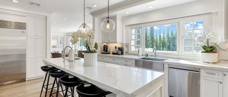 A modern kitchen with a large island, stainless steel appliances, and a view of the outdoors.