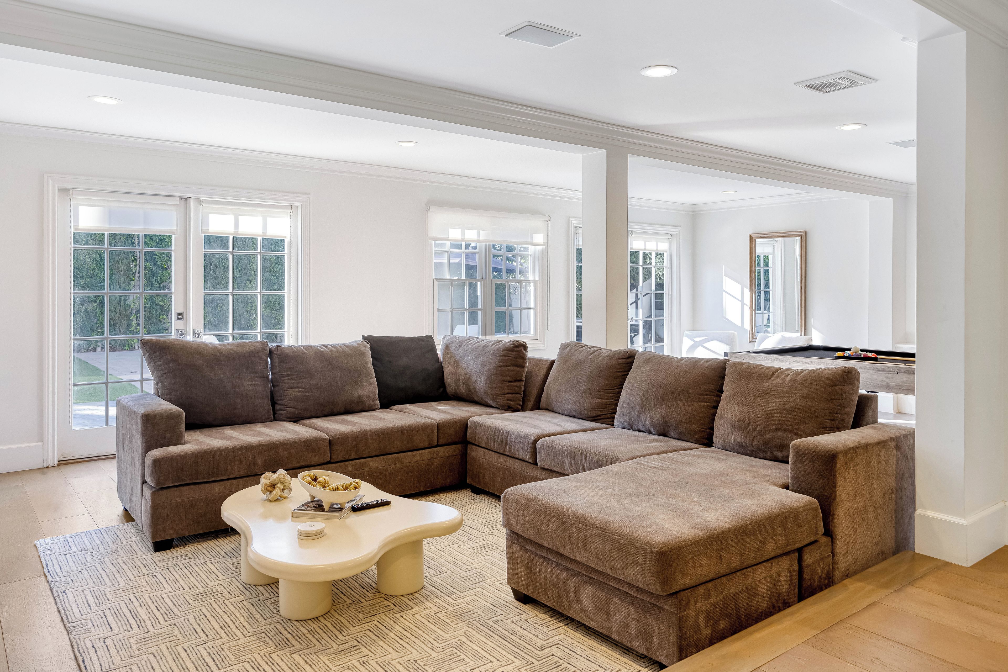 A spacious living room with a sectional sofa, a coffee table, and a pool table.