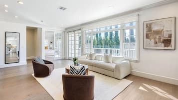 Un salon spacieux avec une grande fenêtre, un canapé blanc, deux fauteuils marron et une table basse ronde.