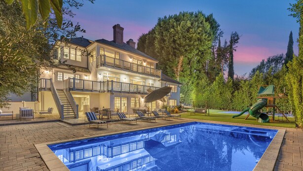 A large two-story house with a swimming pool, outdoor seating, and a well-maintained garden.