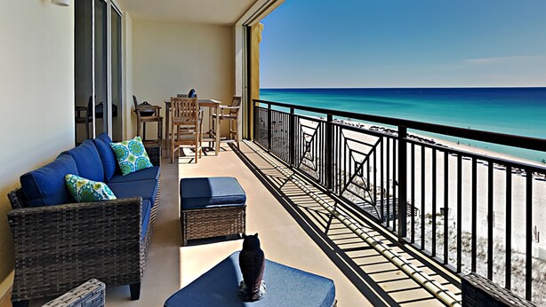 Un balcone con vista sulla spiaggia, mobili in vimini, un divano blu e una piccola statua.