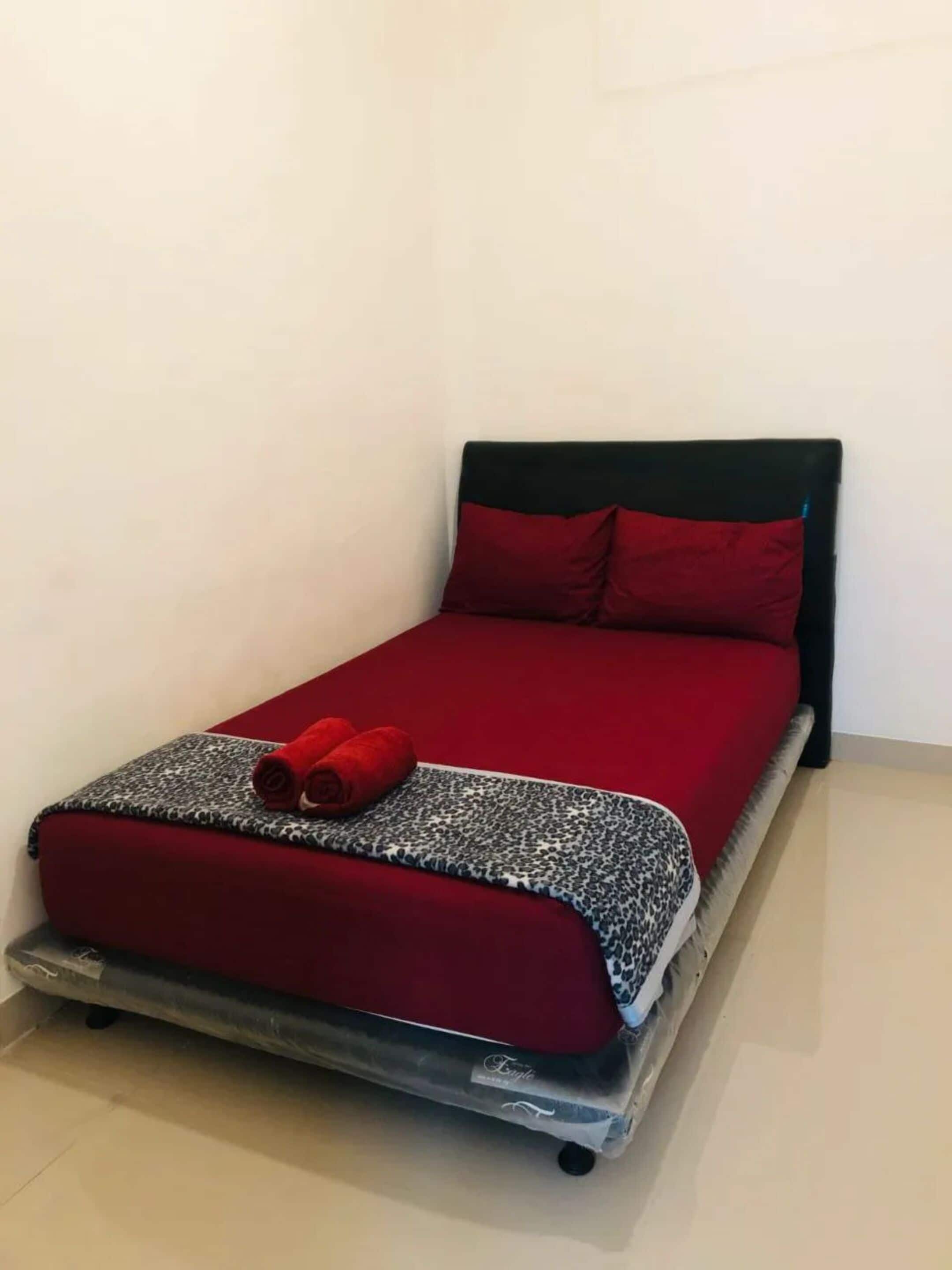 A single bed with a red mattress and pillows, a leopard print blanket, and two red towels.