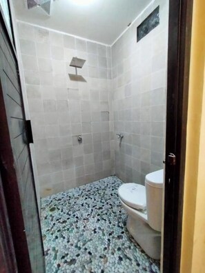 A small, tiled bathroom with a shower, toilet, and a tiled floor. - Homestay Calliandra (Banyuwangi)