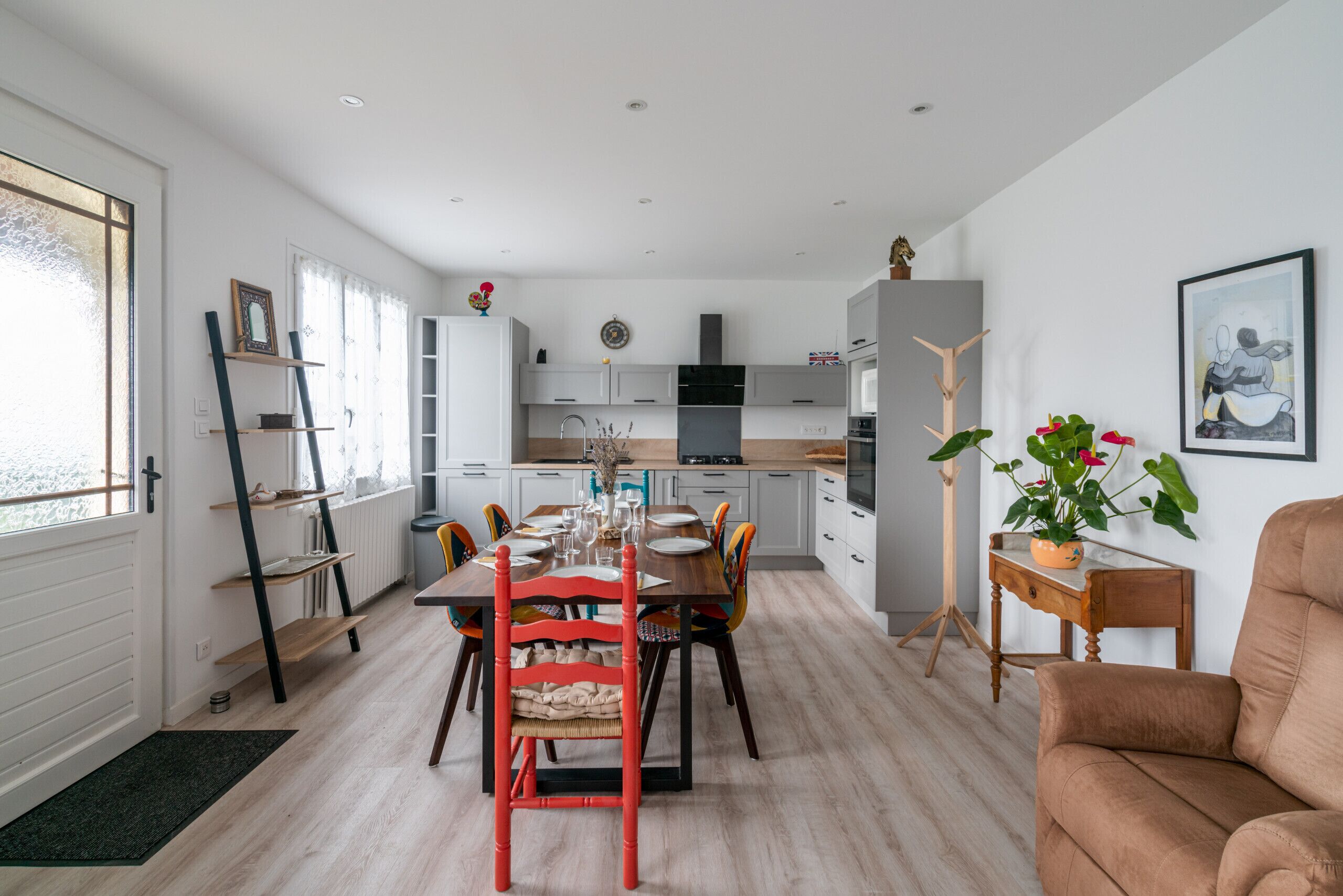 Een moderne keuken met witte kasten, een eettafel met rode stoelen en een houten vloer.