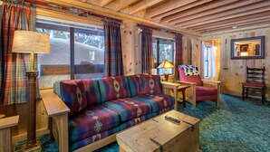 A cozy cabin interior with a wooden ceiling, plaid curtains, a colorful sofa, a small table, and a chair. - Summer special, stay before 9/8/26 get third night half off. (Government Camp)