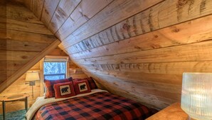 A cozy bedroom with a checkered bedspread, a lamp, and a window with a view of trees. - Summer special, stay before 9/8/26 get third night half off. (Government Camp)