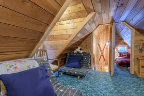 A cozy attic bedroom with a sloped ceiling, a bed with a red and blue plaid comforter, a small sofa with patterned cushions, and a teddy bear on the sofa. - Government Camp, still available for July 4th, 3rd night free ! (Government Camp)