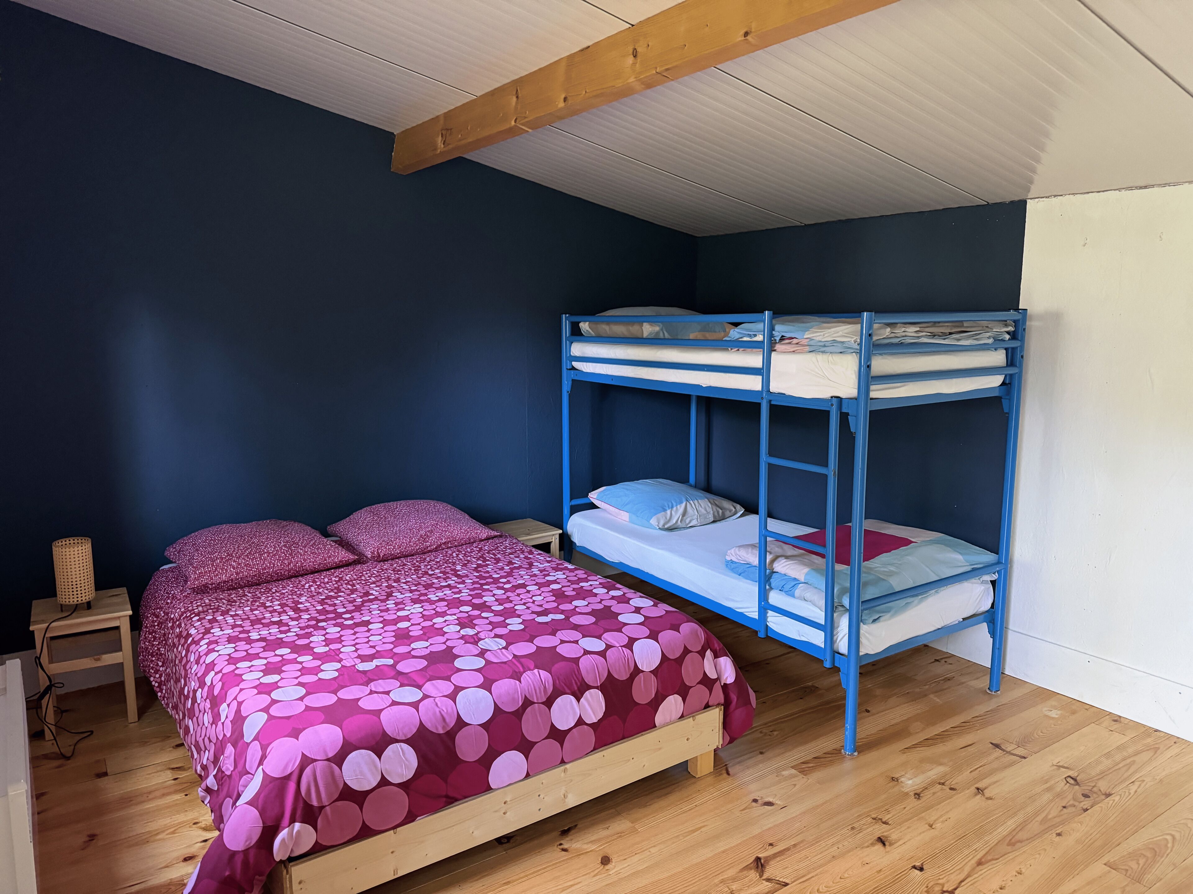 Una habitación con una litera, una cama individual con colcha estampada, una mesita de noche de madera y una lámpara.