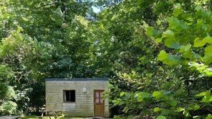A small wooden cabin with a door and windows, surrounded by trees and a gravel path. - Etretat Aventure (Les Loges)