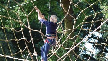 A person navigating a rope bridge in an outdoor setting with trees in the background.