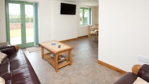 A living room with a brown leather sofa, a wooden coffee table, and a television mounted on the wall. - Country Views peaceful location in superb setting close to the Norfolk Broads (Loddon)