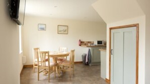 A dining area with a wooden table and chairs, a kitchen in the background, and a door on the right. - Country Views peaceful location in superb setting close to the Norfolk Broads (Loddon)