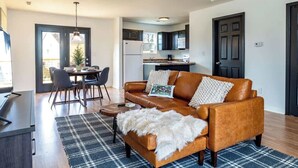 A modern living room with a leather sofa, a dining table with chairs, and a kitchen area in the background.