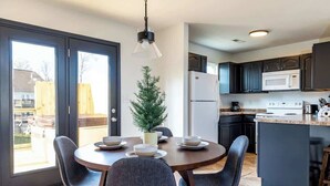 A modern kitchen with dark cabinets, a central island, and a dining area with chairs.