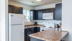 A modern kitchen with dark cabinets, a white refrigerator, a microwave, a stove, and a granite countertop.