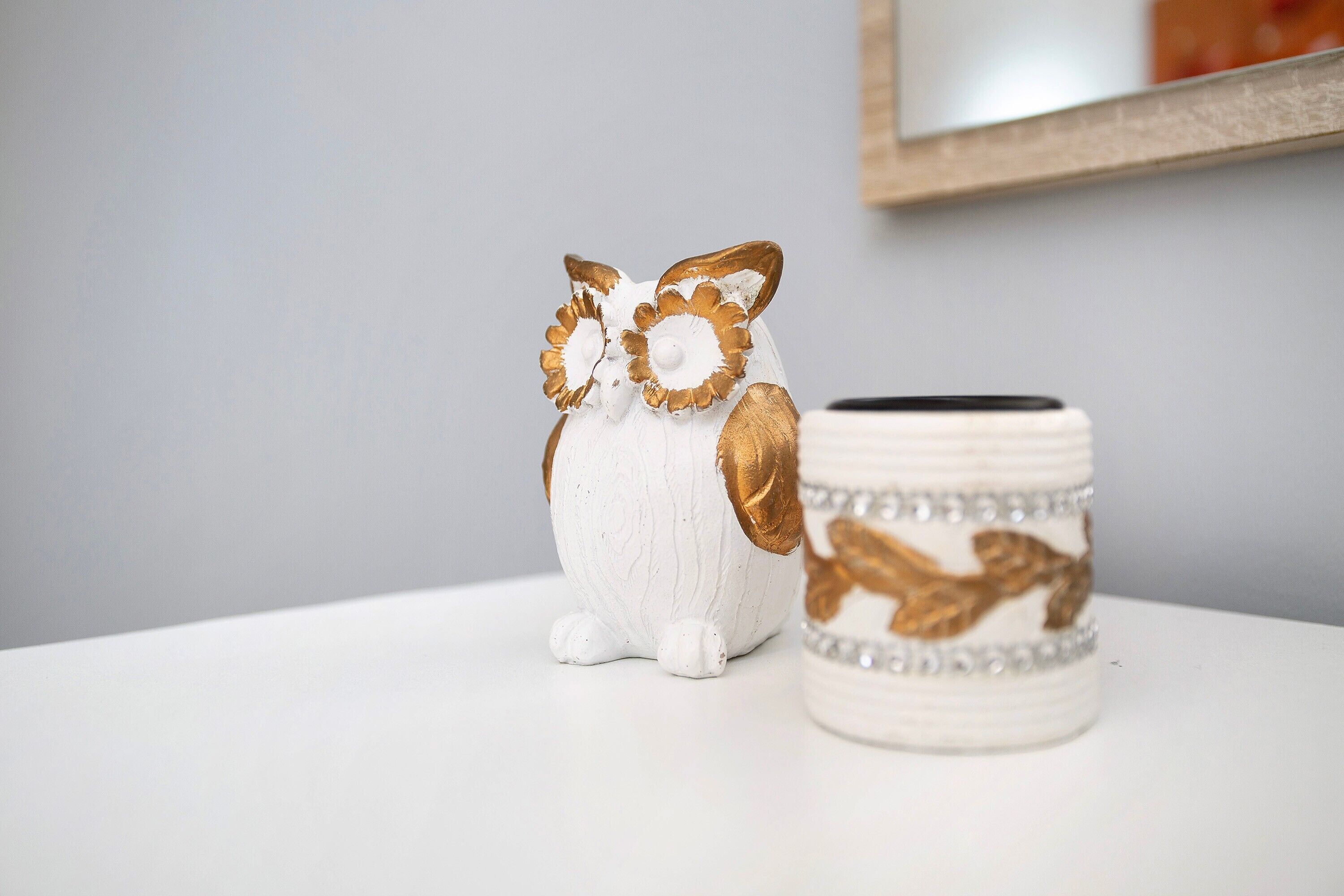 A white ceramic owl figurine and a white ceramic mug with gold and silver designs on a white surface.