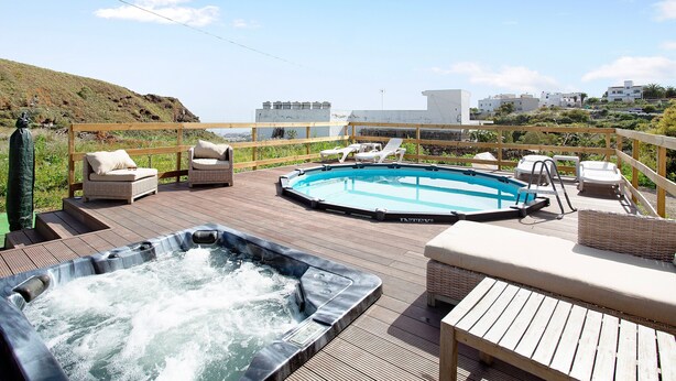 A rooftop pool area with hot tubs, lounge chairs, and a view of the surrounding landscape.