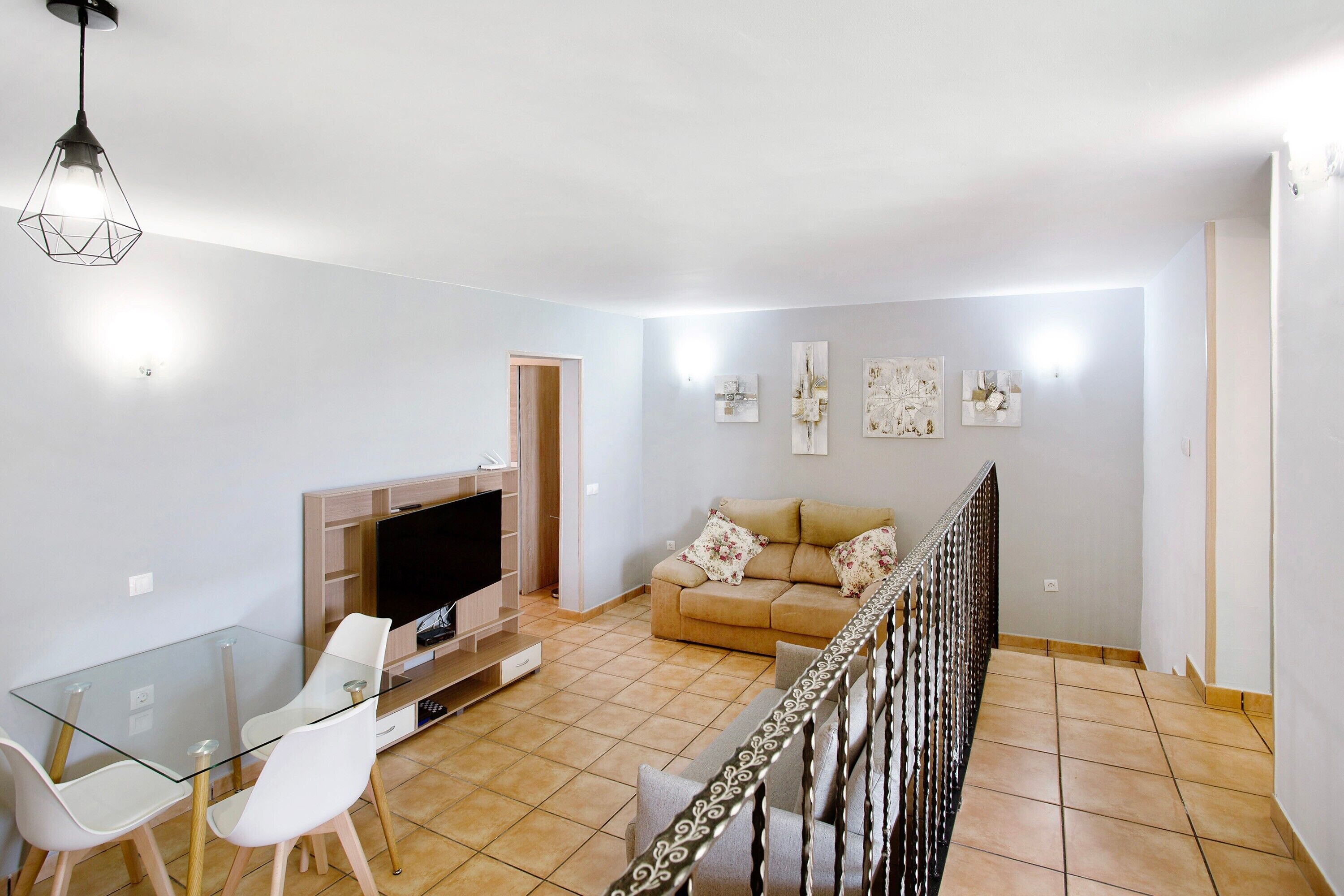 Una sala de estar con una mesa de vidrio, sillas blancas, un sofá y un televisor.