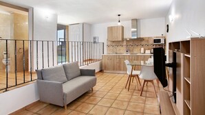A modern apartment with a living area featuring a sofa, a dining table with chairs, a kitchen with wooden cabinets, and a TV.