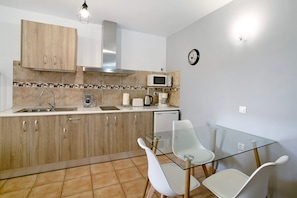 Una cocina compacta con microondas, lavamanos y mesa de vidrio con sillas.