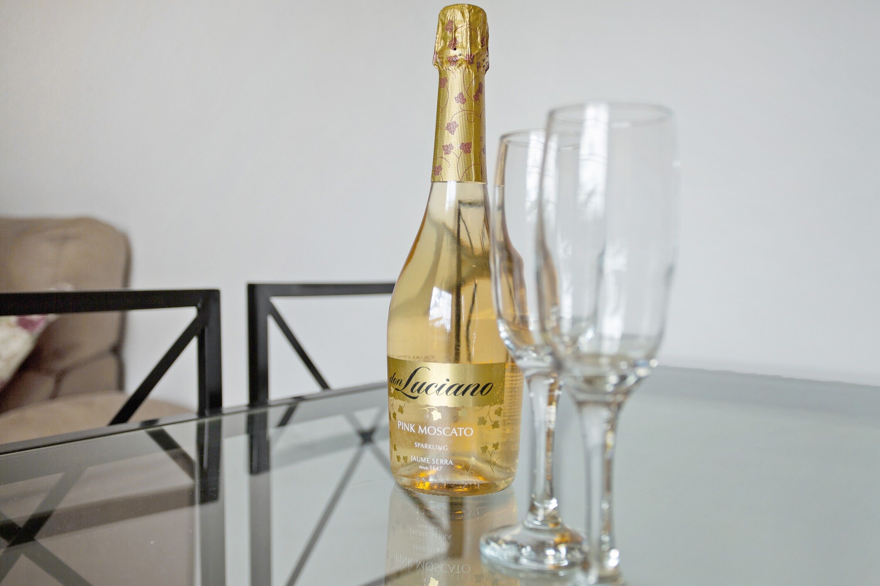 Una botella de vino espumoso rosado Luciano Pink Moscato sobre una mesa de vidrio, con una copa transparente a su lado.