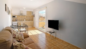 A living room with a sofa, a TV, and a dining area with chairs and a table.