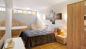 A bedroom with a bed, nightstand, lamp, wardrobe, and a bathroom with a bathtub and sink.