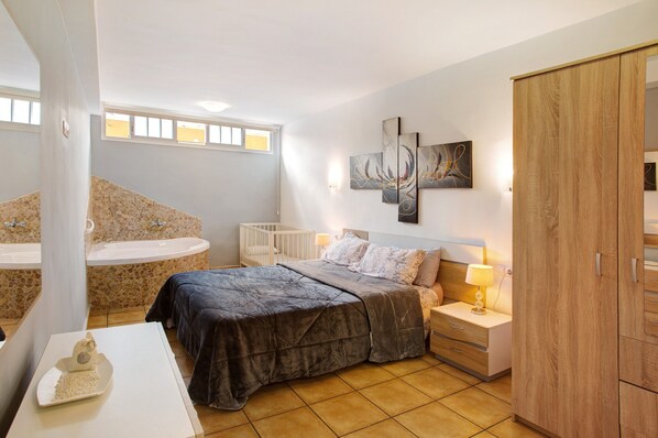 Une chambre à coucher comprenant un lit, une table de chevet, une lampe, une armoire, ainsi qu’une salle de bain avec une baignoire et un lavabo.