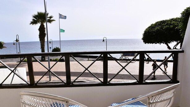 A balcony with two wicker chairs, a railing, and a view of the sea.