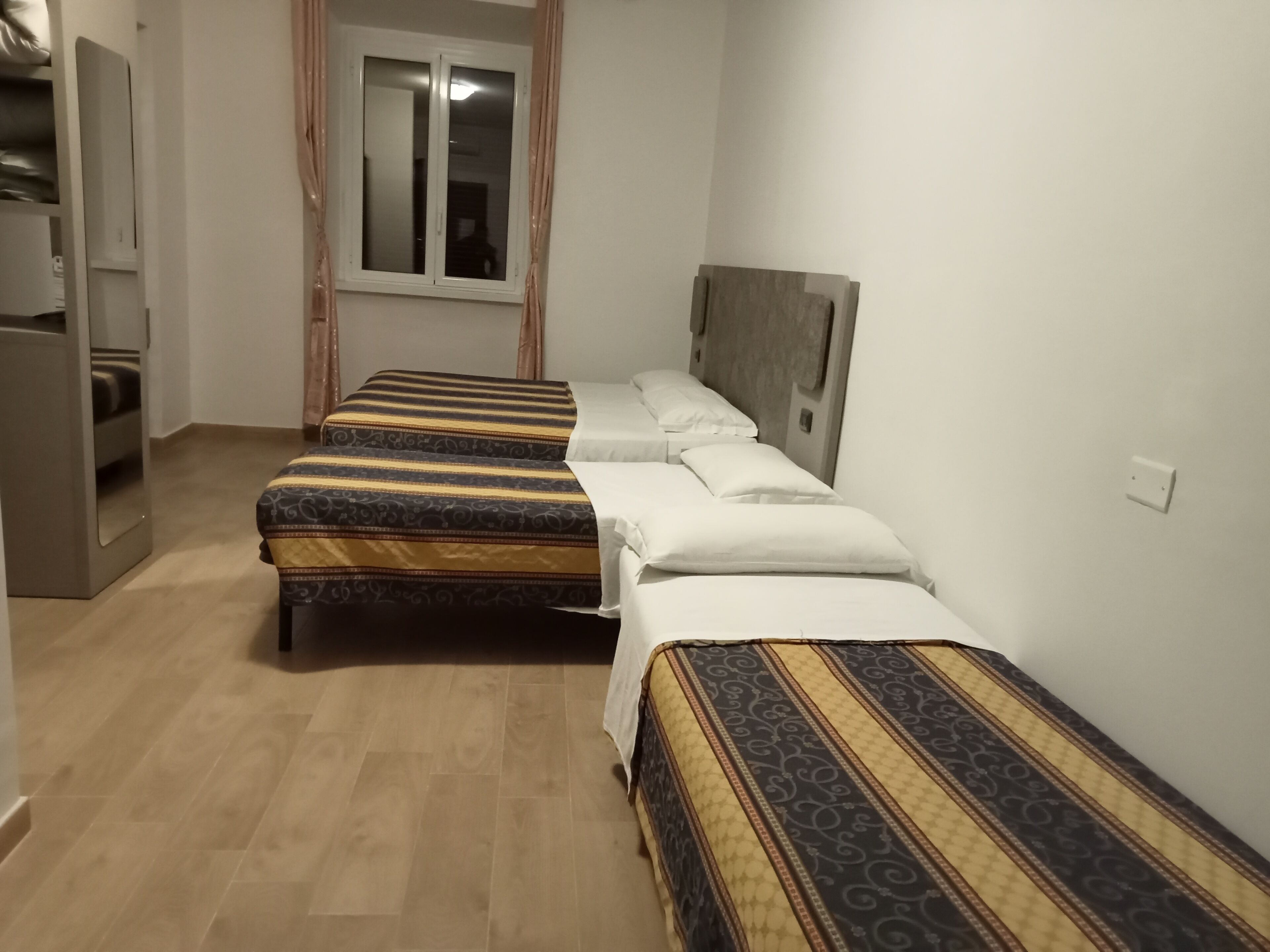 A hotel room with two single beds, a wardrobe, a window, and a door.