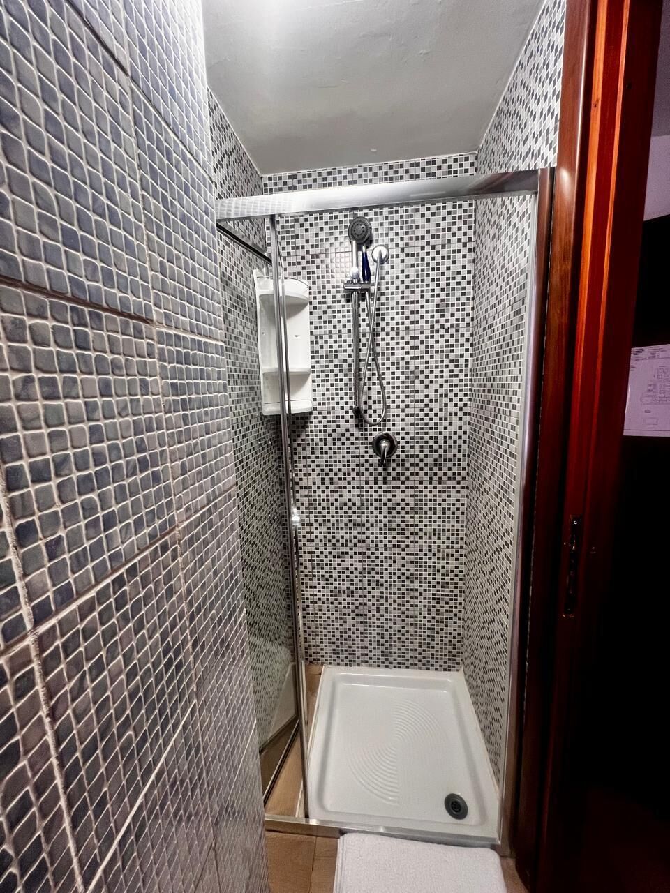 A small bathroom with a shower, tiled walls, and a white sink.