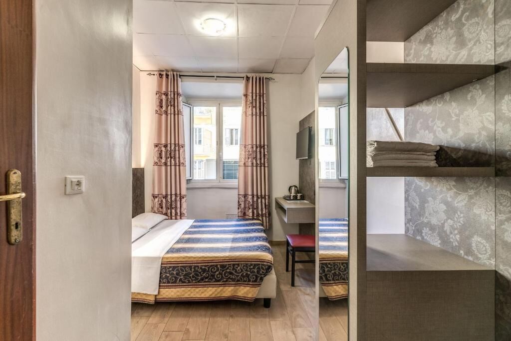 A bedroom with a bed, a desk, a chair, and a window with curtains.
