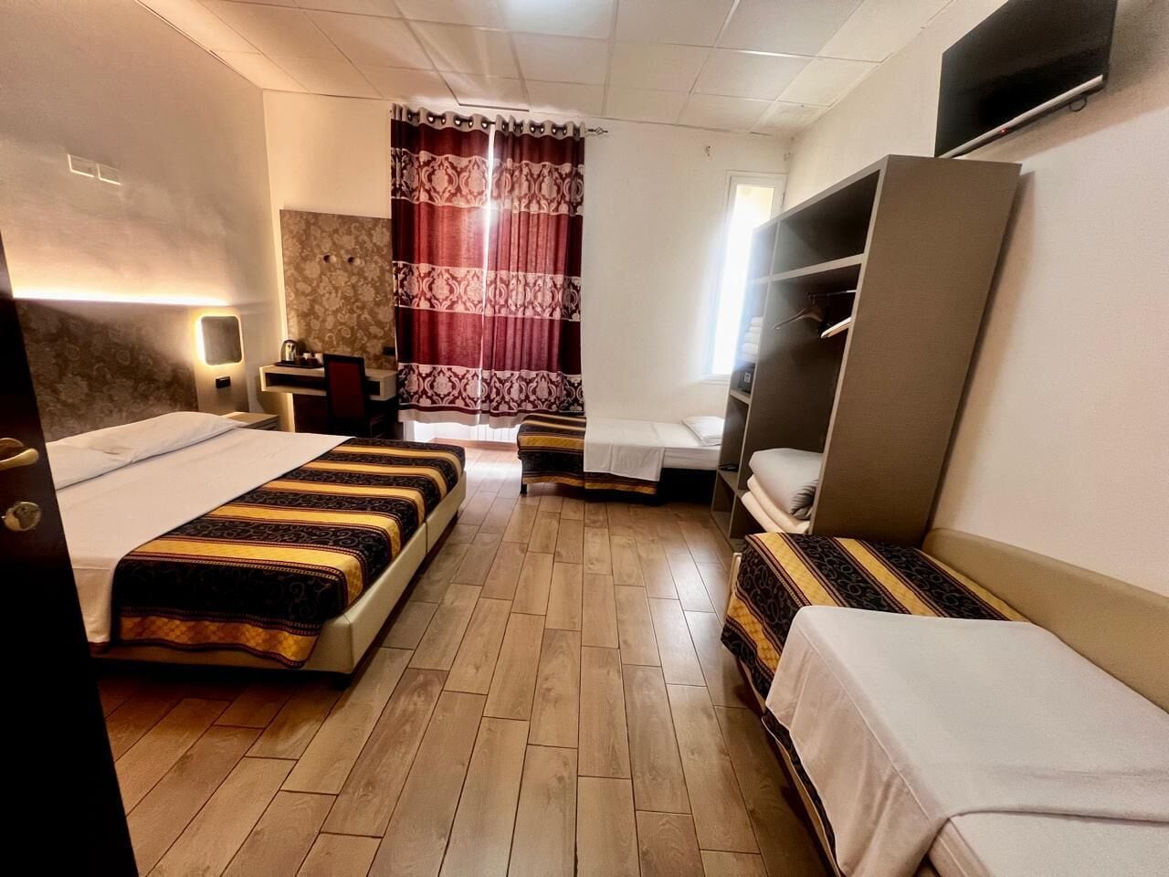 A hotel room with two beds, a wardrobe, a TV, and a window with curtains.