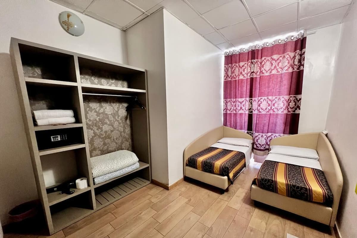 A room with two beds, a wardrobe, and a window with a curtain.