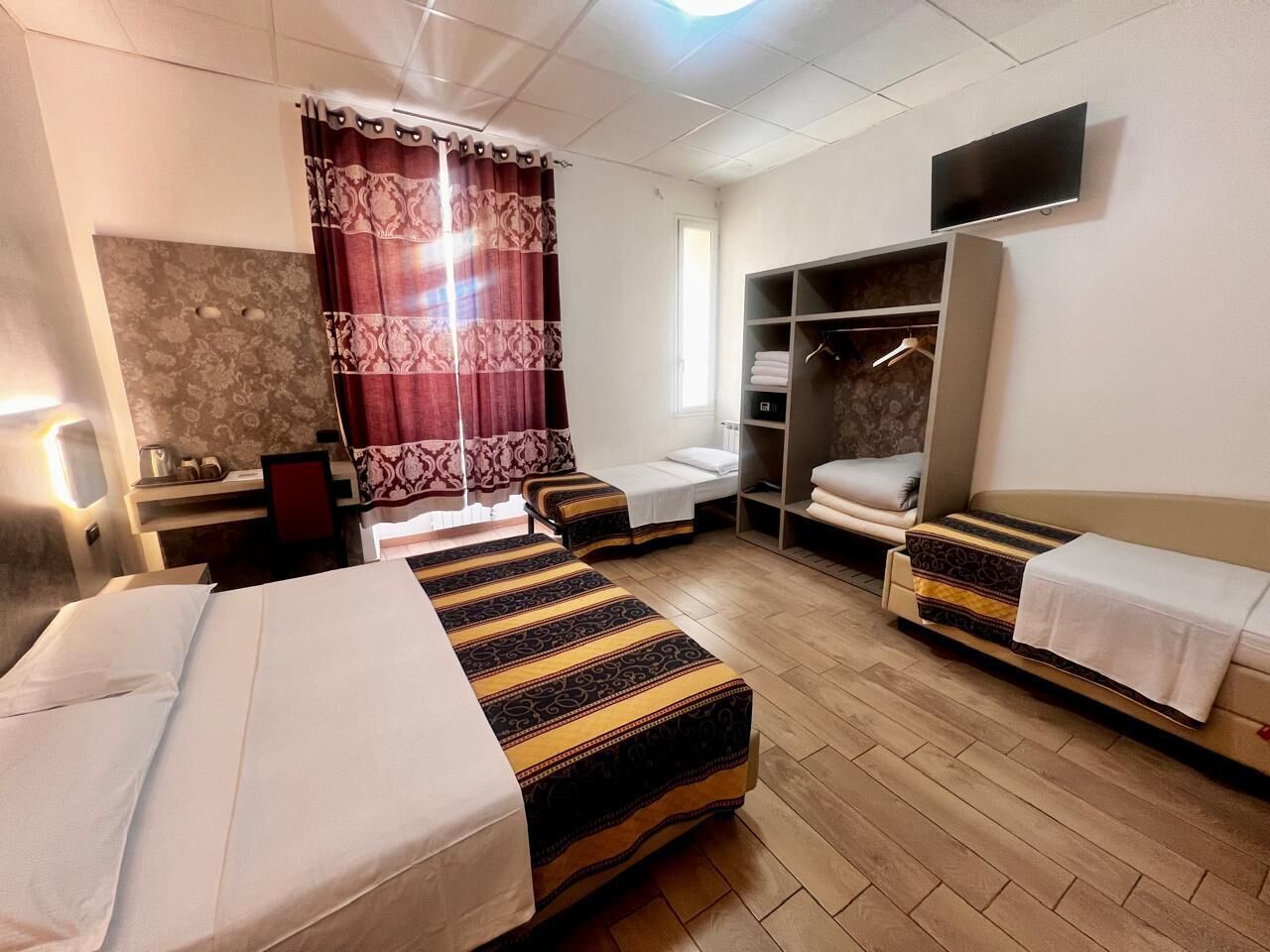 Habitación de hotel con dos camas, un armario, un televisor y un escritorio con una silla.
