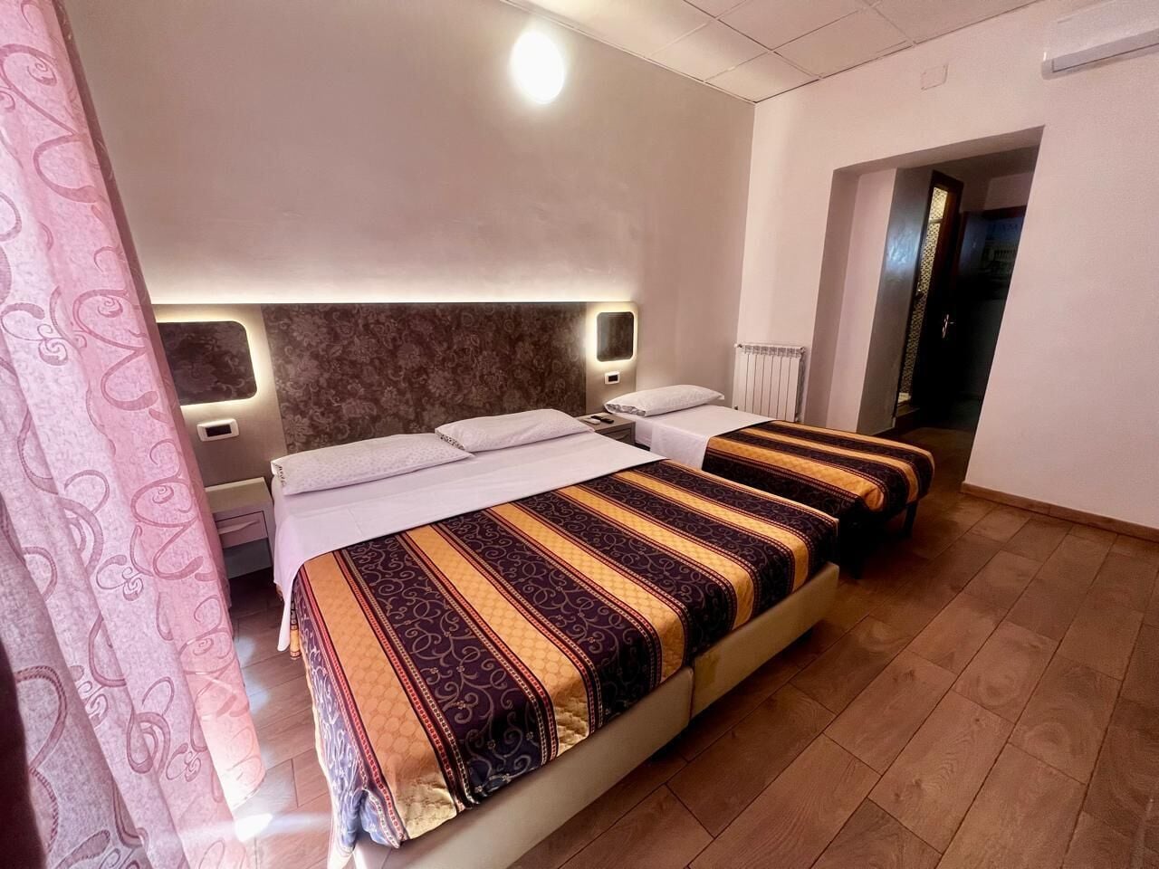 Une chambre d’hôtel avec un grand lit, des tables de chevet, une tête de lit et une porte donnant sur une autre pièce.