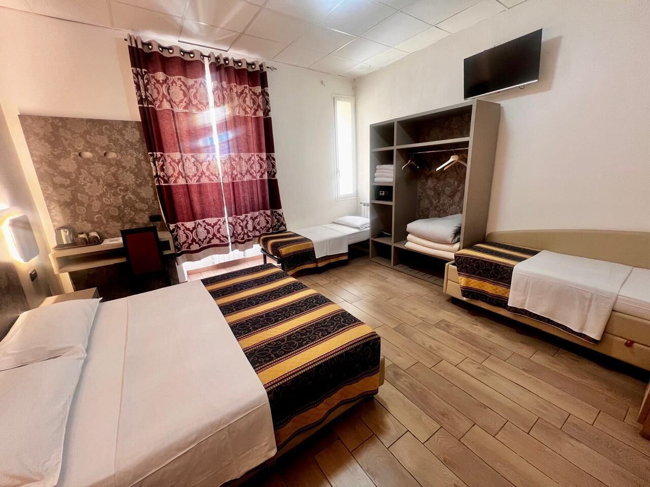 A hotel room with two beds, a wardrobe, a TV, and a window with curtains.