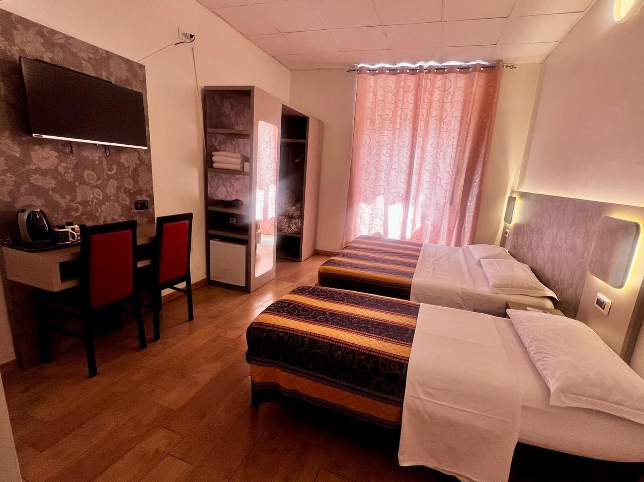 A hotel room with a desk, two beds, a wardrobe, and a shower area.