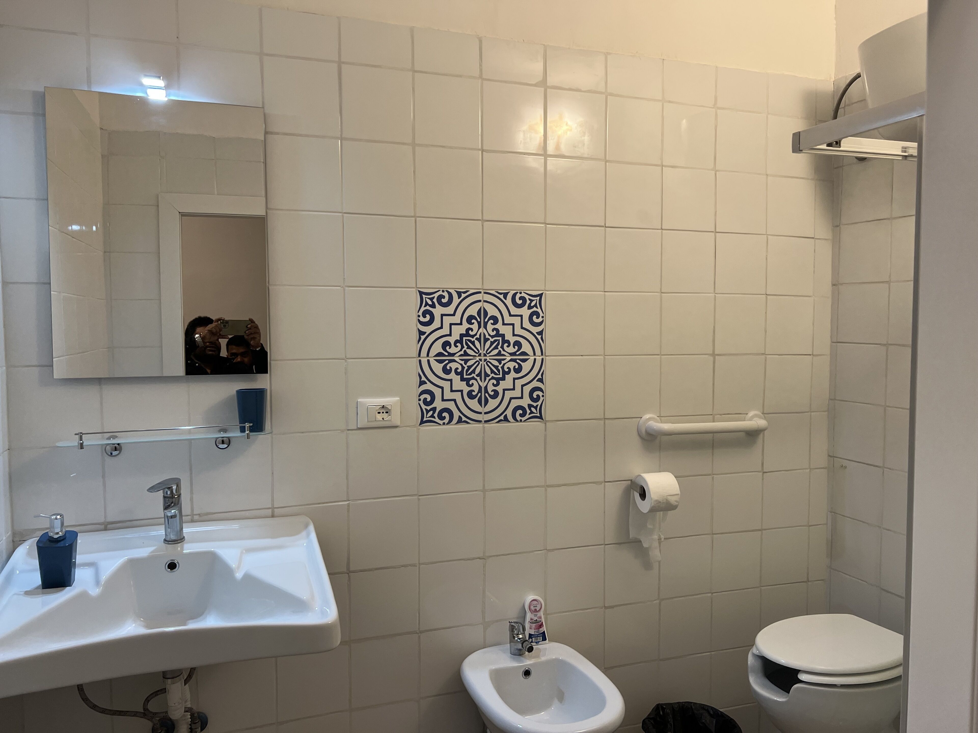 A bathroom with a white sink, bidet, toilet, and a decorative tile pattern on the wall.