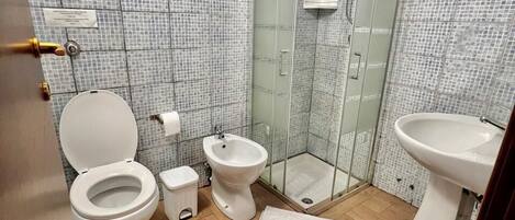 A bathroom with a toilet, bidet, sink, and glass shower enclosure.