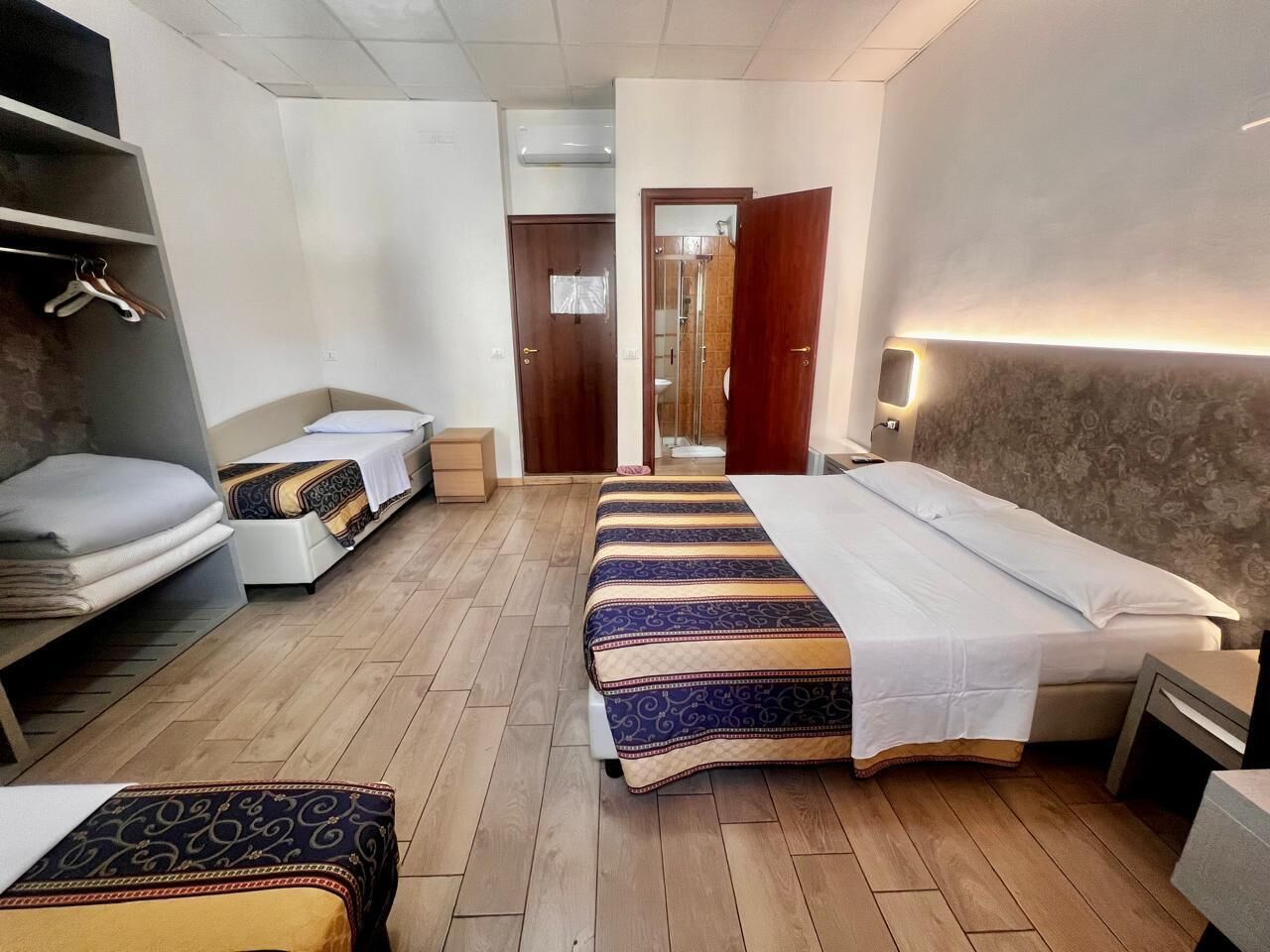 A hotel room with two beds, a wardrobe, a bedside table, and a shower area.